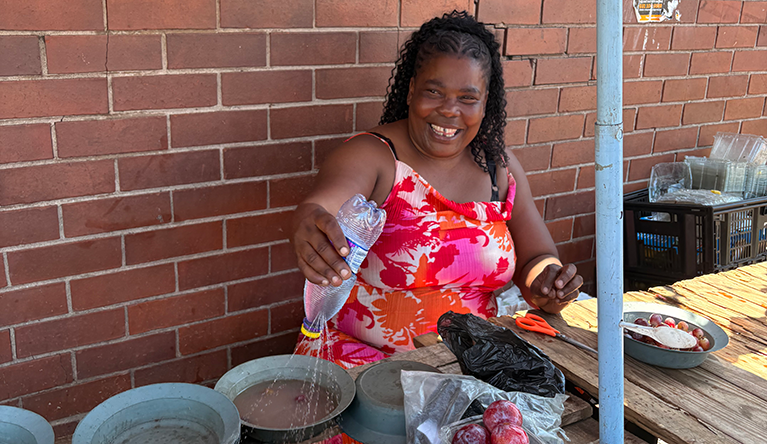 Between beach brollies and a makeshift sprinkler, fruit trader Nomusa Luthuli protects herself and her stock from the sun which can pummel the delicate plums she’s selling today. Picture: Leonie Joubert
