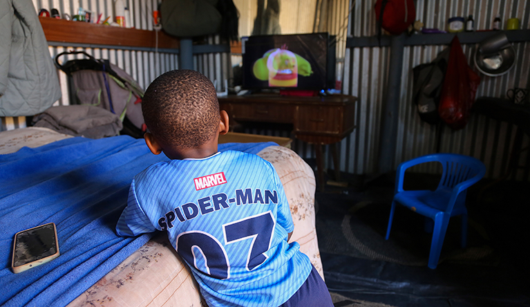 A young boy, unable to walk, watches cartoons at his home in KuGompo City, East London. Photograph: Mark Andrews/SA|AJP
