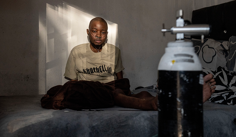 John Gahle sits on his bed beside his breathing machine and an oxygen tank at his home in Katlehong, east of Johannesburg, South Africa. Gahle must ensure his oxygen tank is always full in case of a power outage. (Photo: Leon Sadiki)